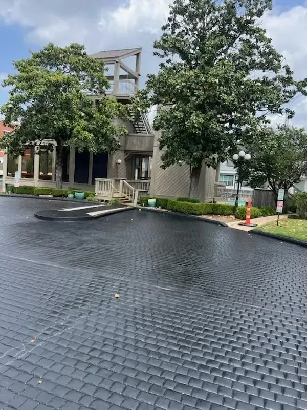 A paved parking area with a building and large trees in the background under a cloudy sky.