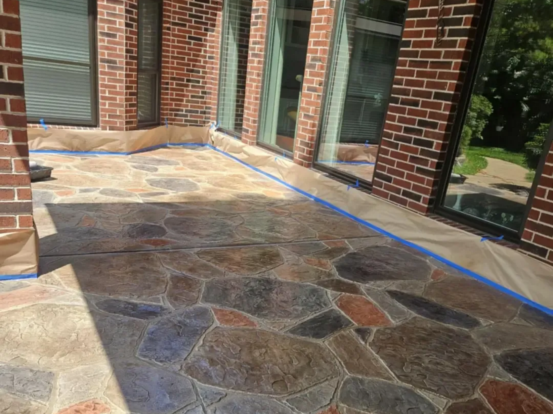 Stamped concrete patio with a stone pattern; brown, blue, and red tones. Brick walls and large windows.