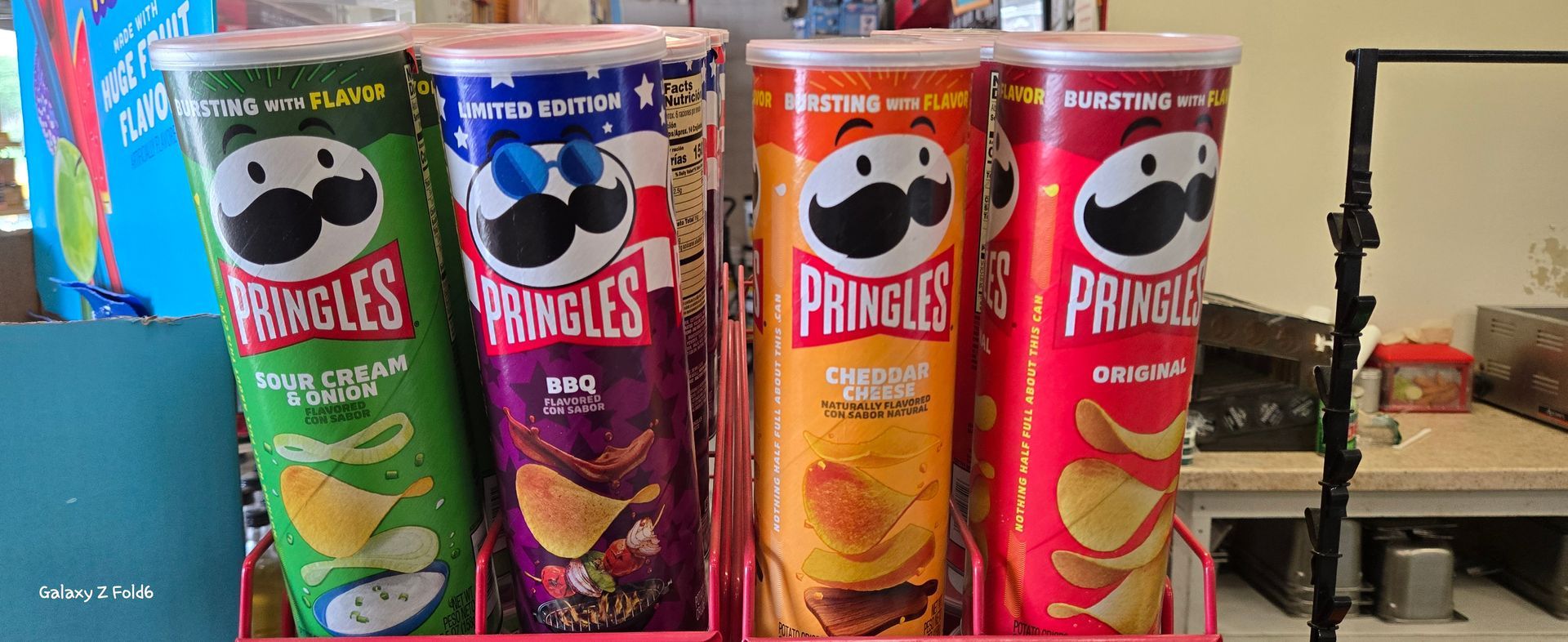 Four cans of pringles chips are lined up on a shelf.