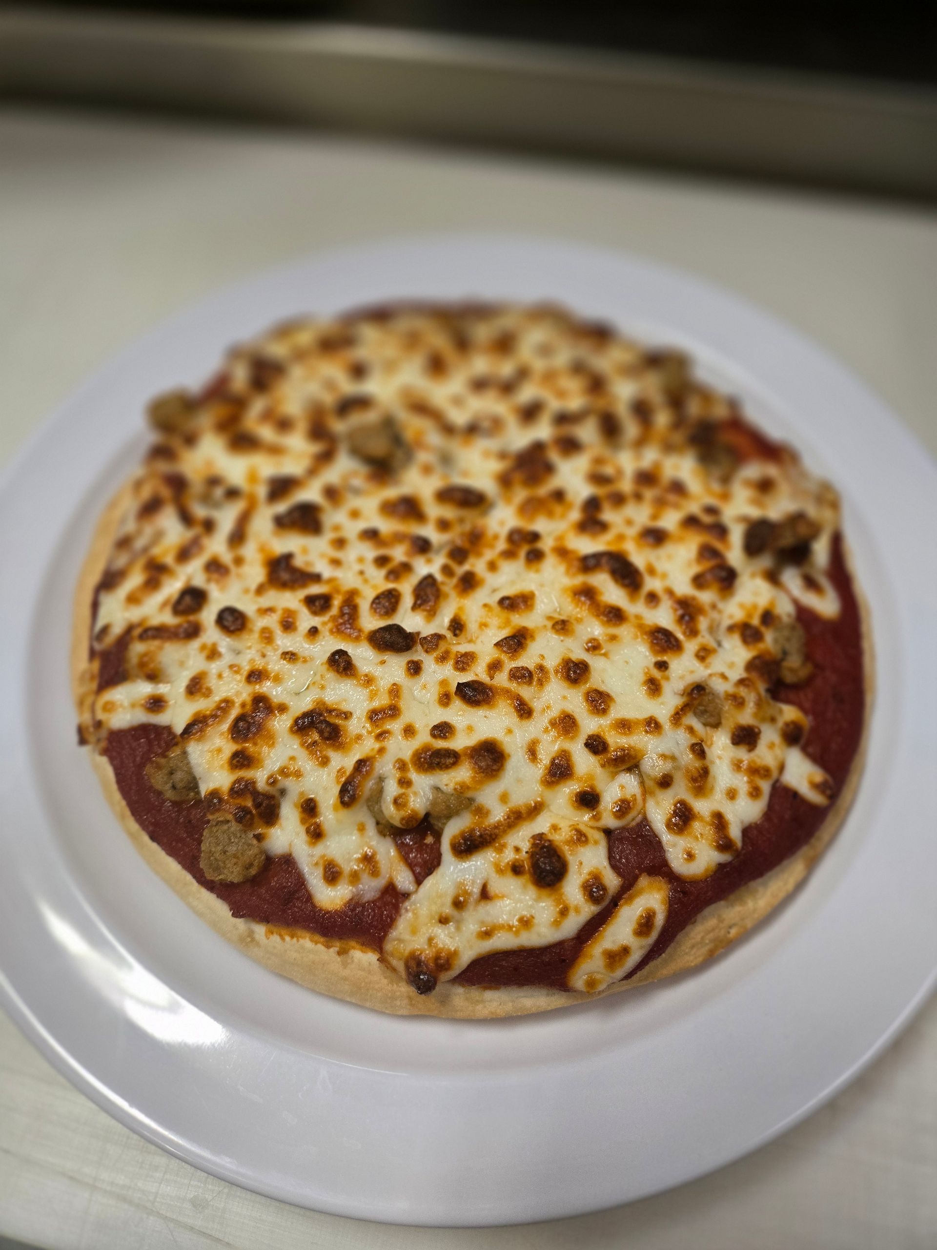 A pizza with cheese and sausage on a white plate.