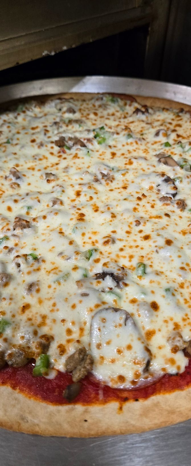 A pizza with a lot of cheese and toppings is sitting on a pan.