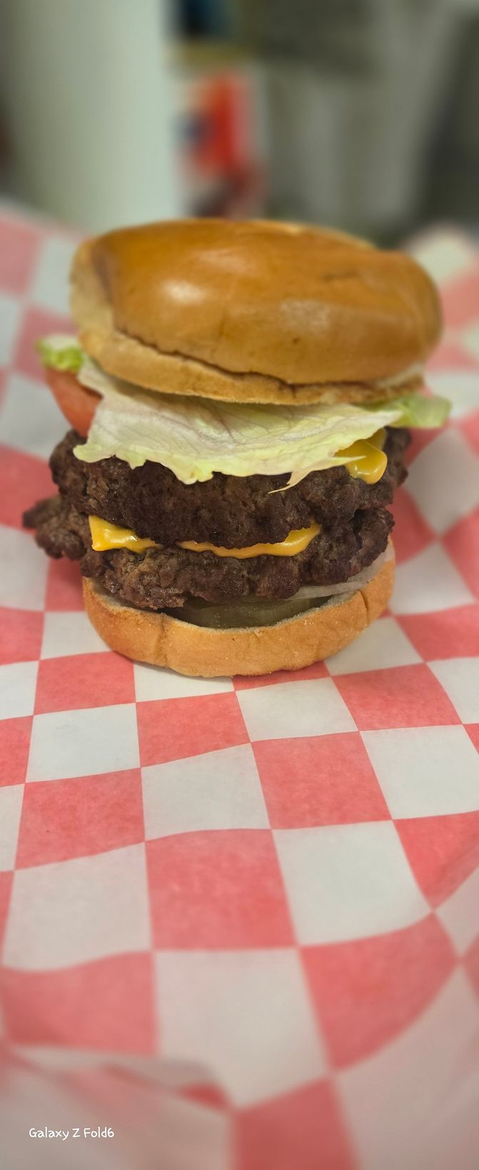A hamburger is sitting on a checkered napkin on a table.