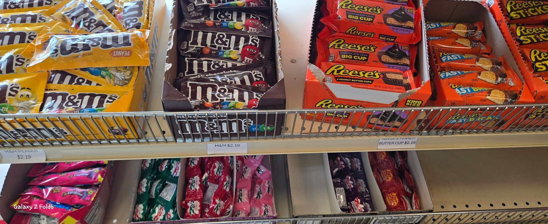 A shelf of candy including m & m 's and reese 's peanut butter cups