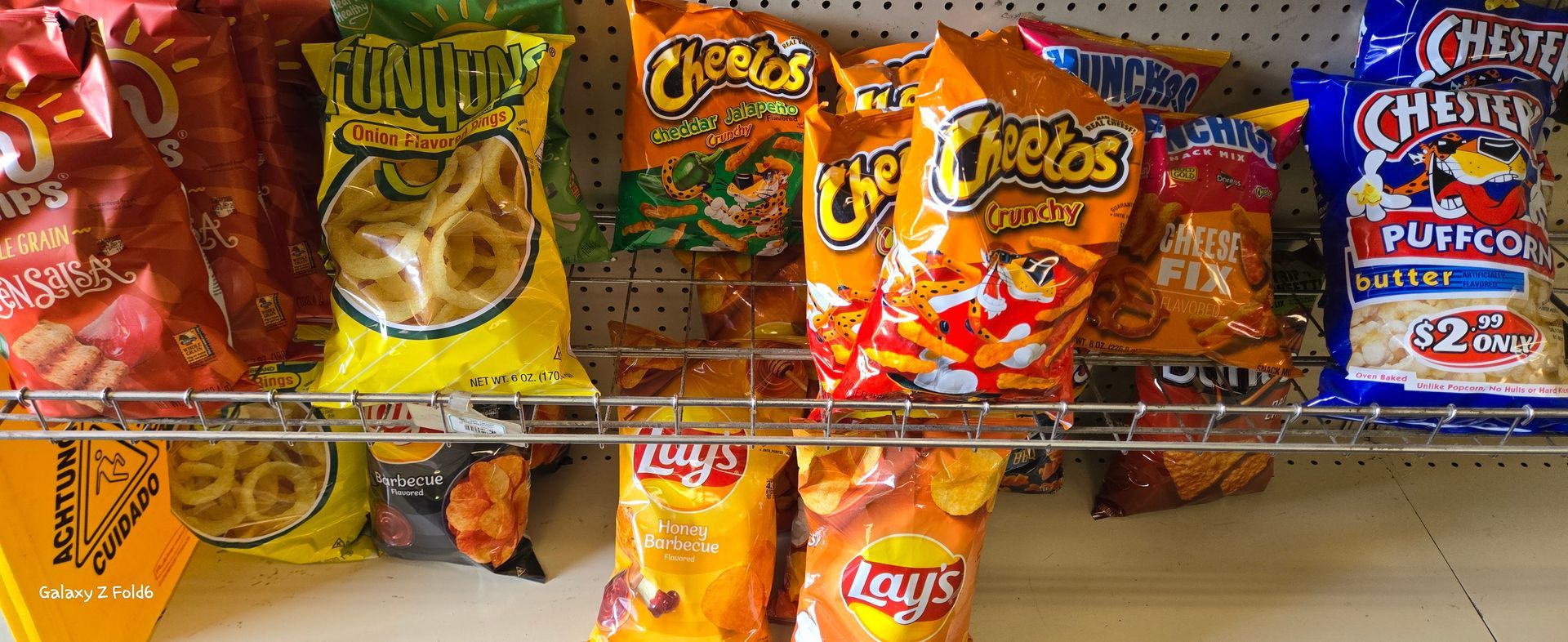 A shelf filled with bags of chips including cheetos and lays.