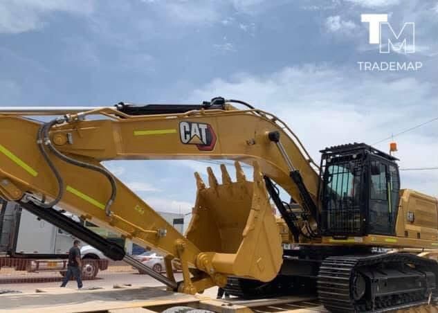 Una excavadora amarilla trabaja en una polvorienta obra en construcción, recogiendo tierra con su pala frontal.