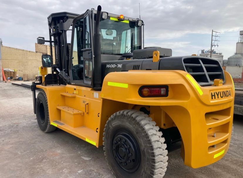 Una grúa amarilla montada sobre un camión de plataforma levanta un contenedor de transporte blanco contra un cielo nublado.