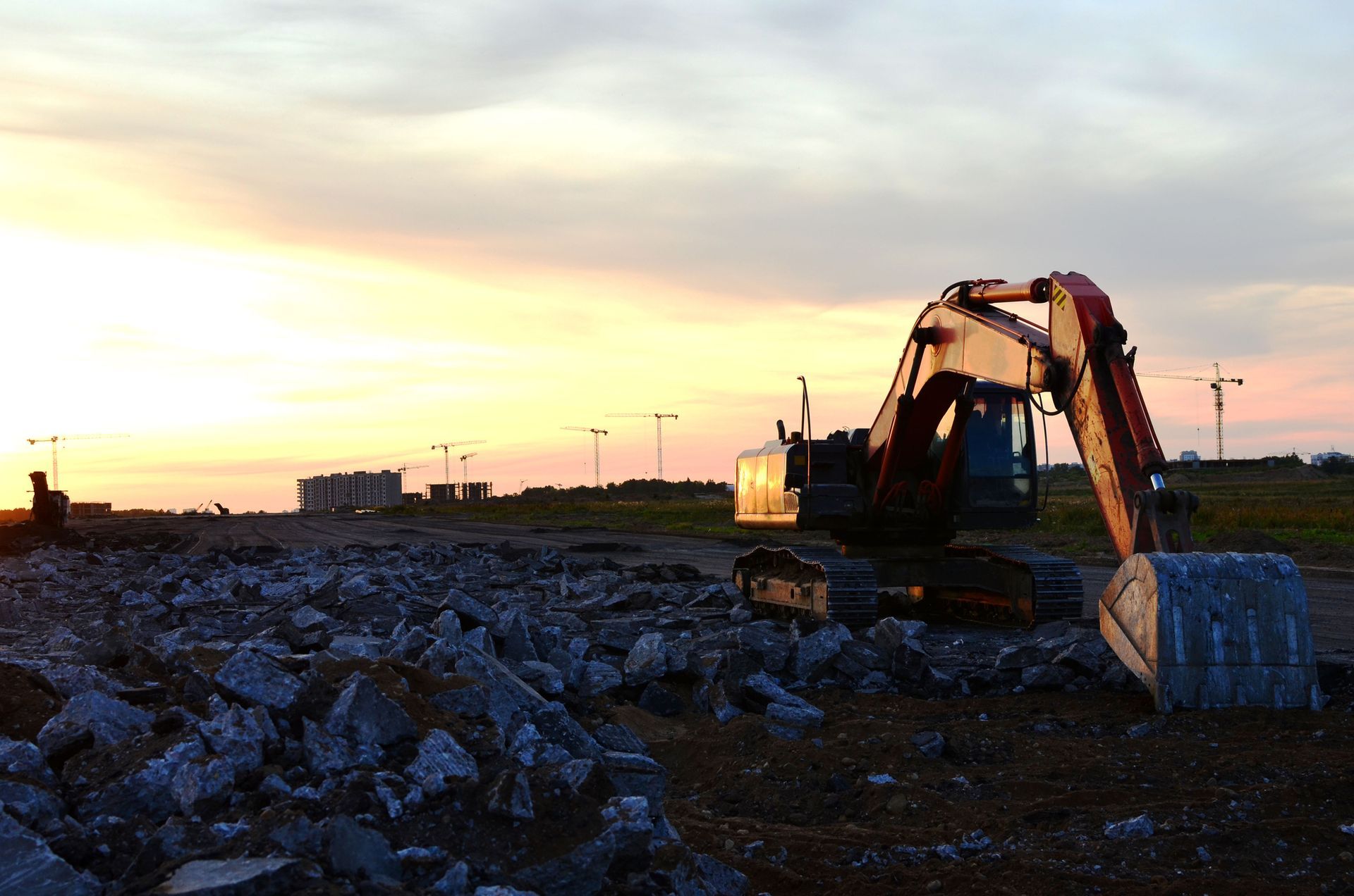 An excavator is sitting in a pile of rocks at sunset.