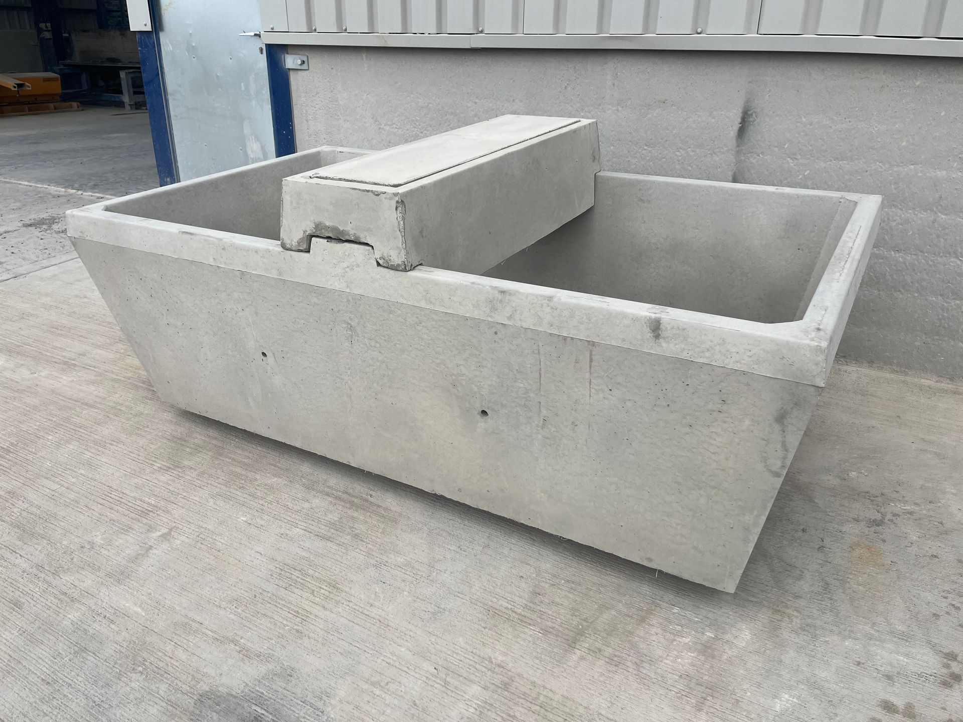 A gray, rectangular concrete livestock water trough sitting outdoors on a paved surface.