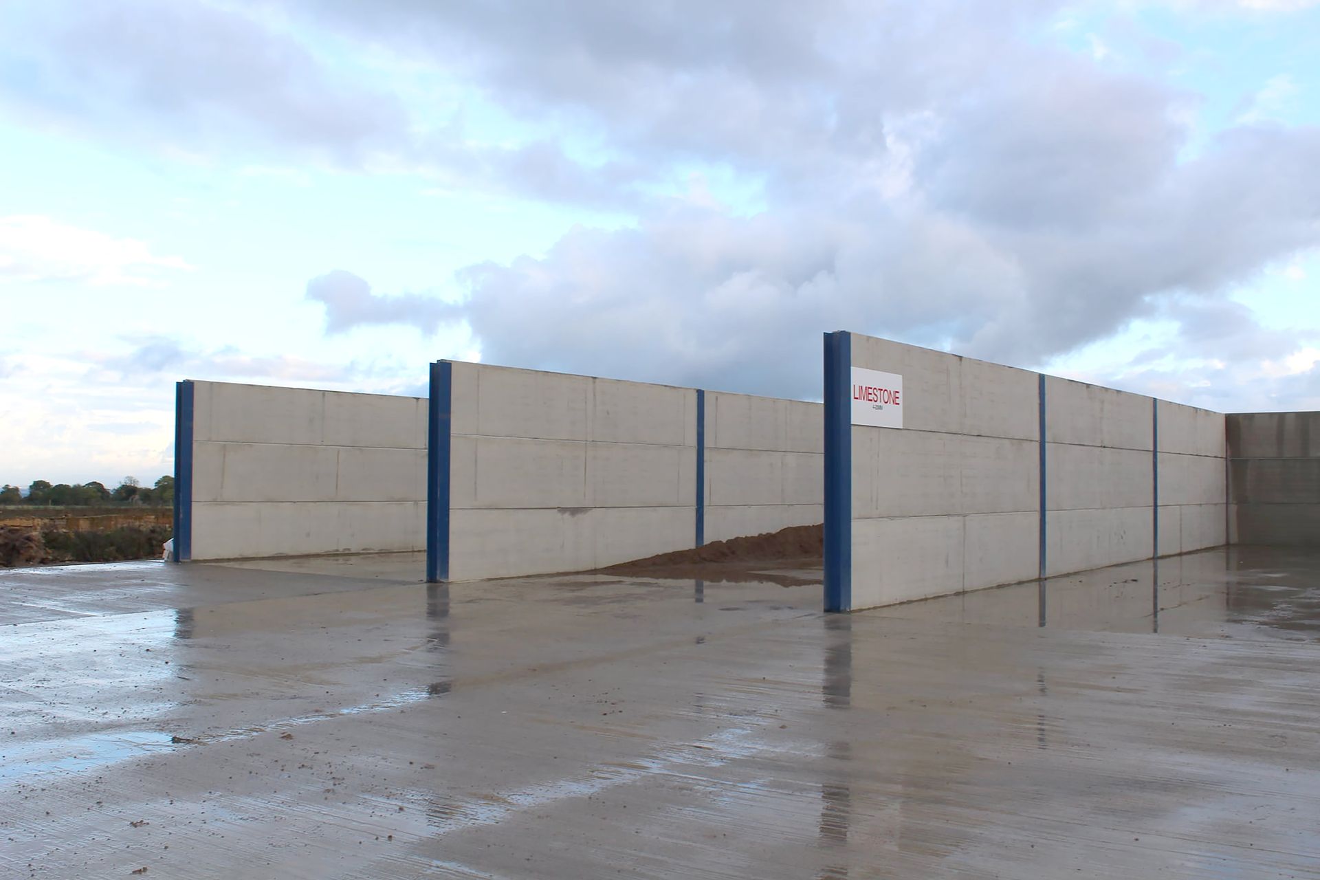 A concrete bunker system with multiple stalls separated by blue vertical steel beams on a wet, paved outdoor surface.