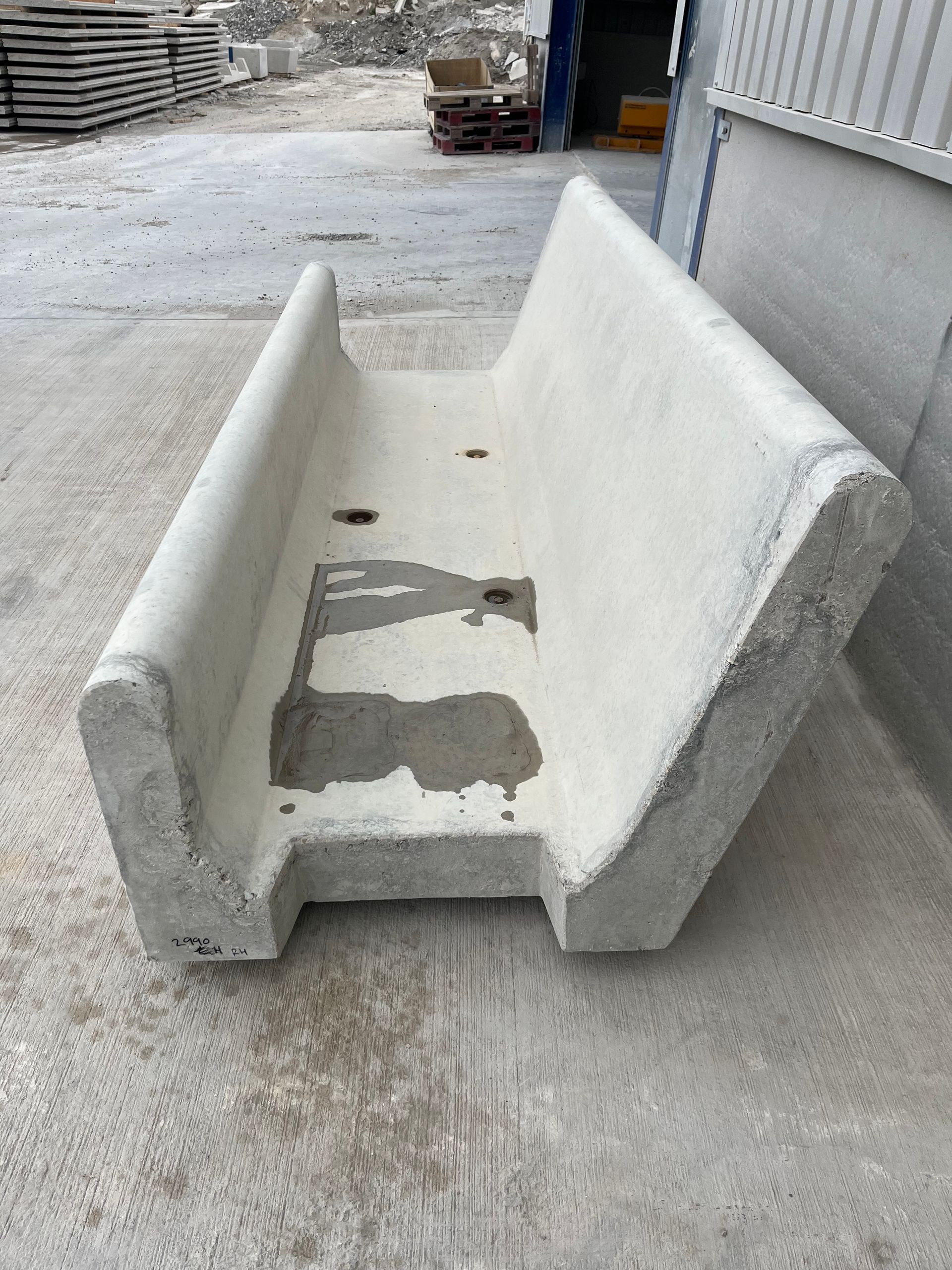 A precast concrete feed trough or barrier unit sitting on a grey paved surface in an industrial yard.