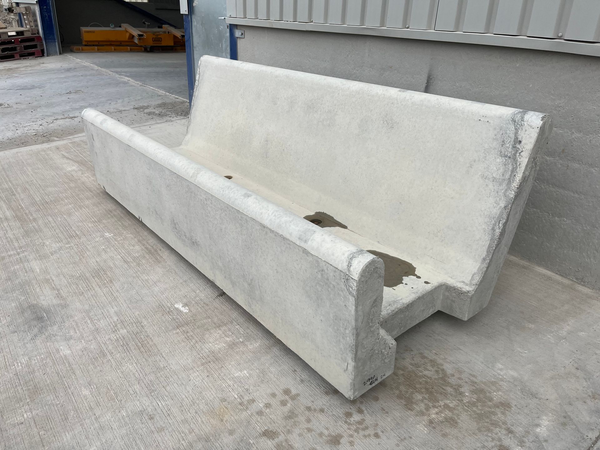 A long, grey concrete trough with a high back, sitting on an outdoor paved surface.