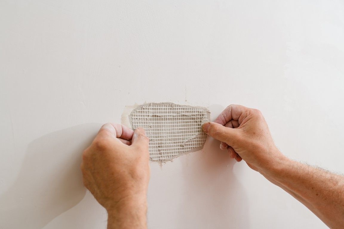 Hands applying mesh patch to a wall, repairing a damaged area.