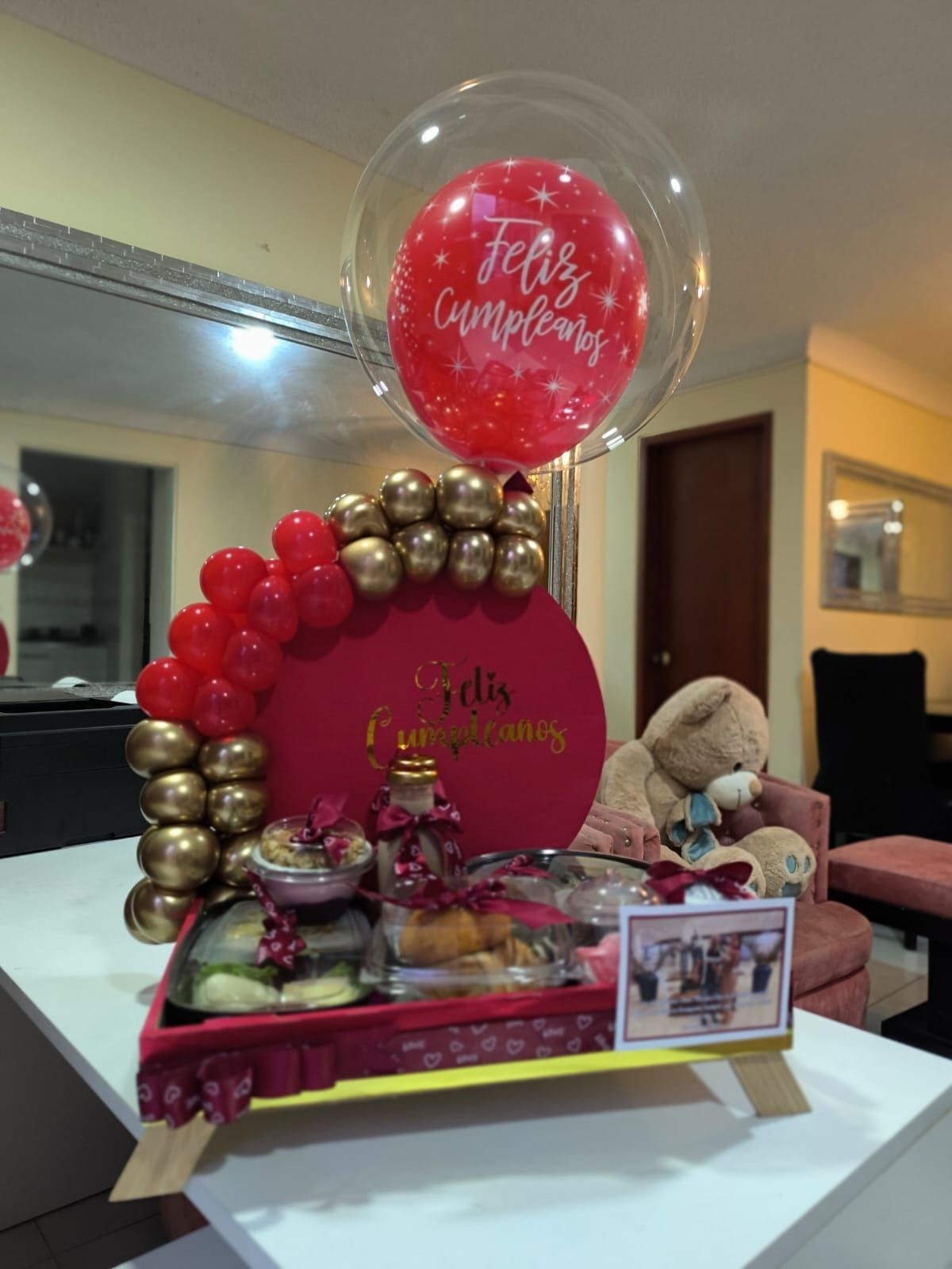 Una bandeja de desayuno con un osito de peluche, globos y la frase