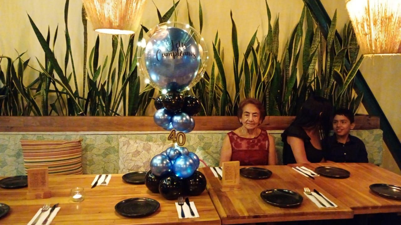 Personas sentadas a una mesa de restaurante, decoraciones de fiesta, globos azules y negros.
