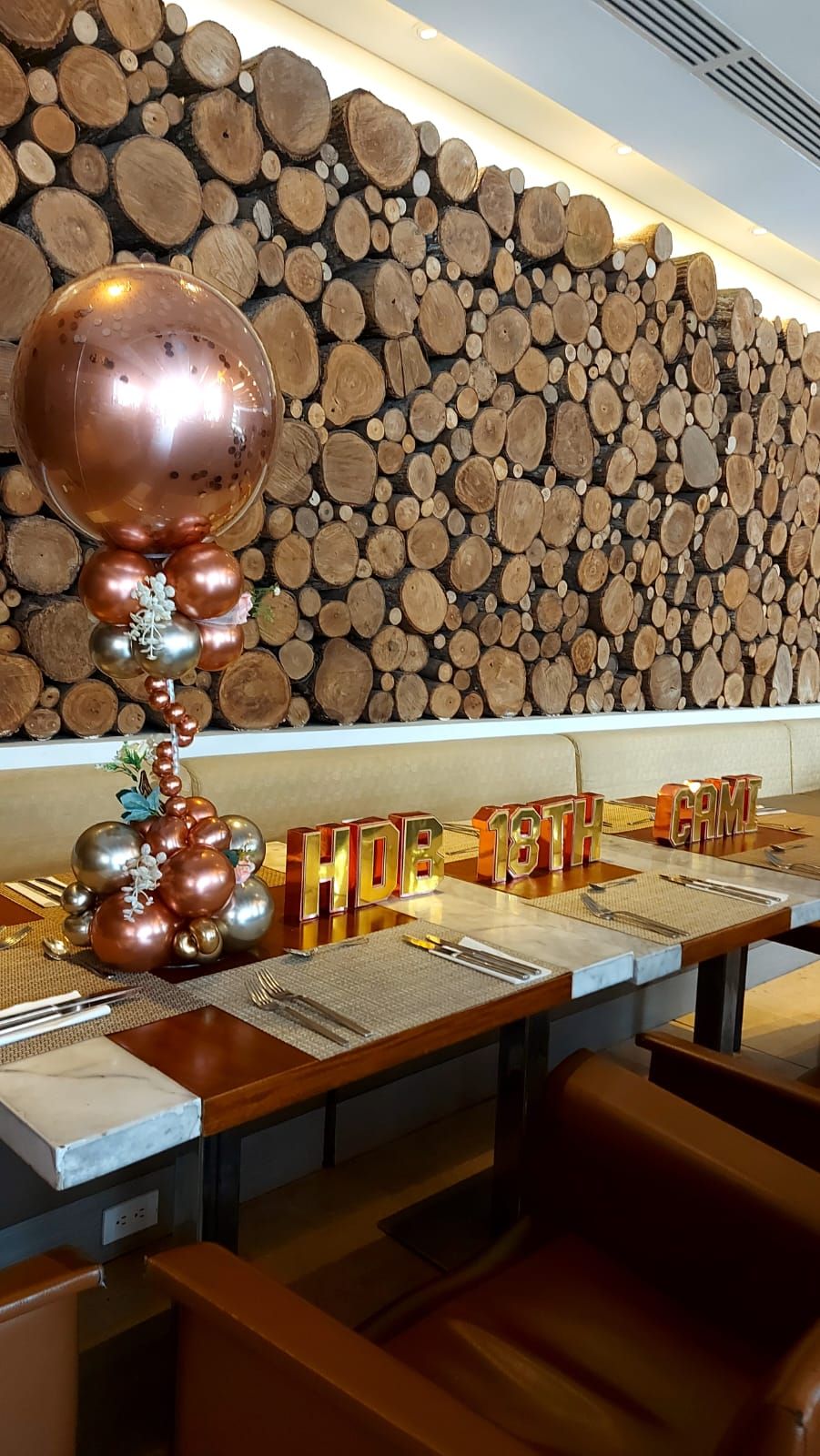 Decoración de mesa de restaurante con globos de cobre y fondo de pared de madera.