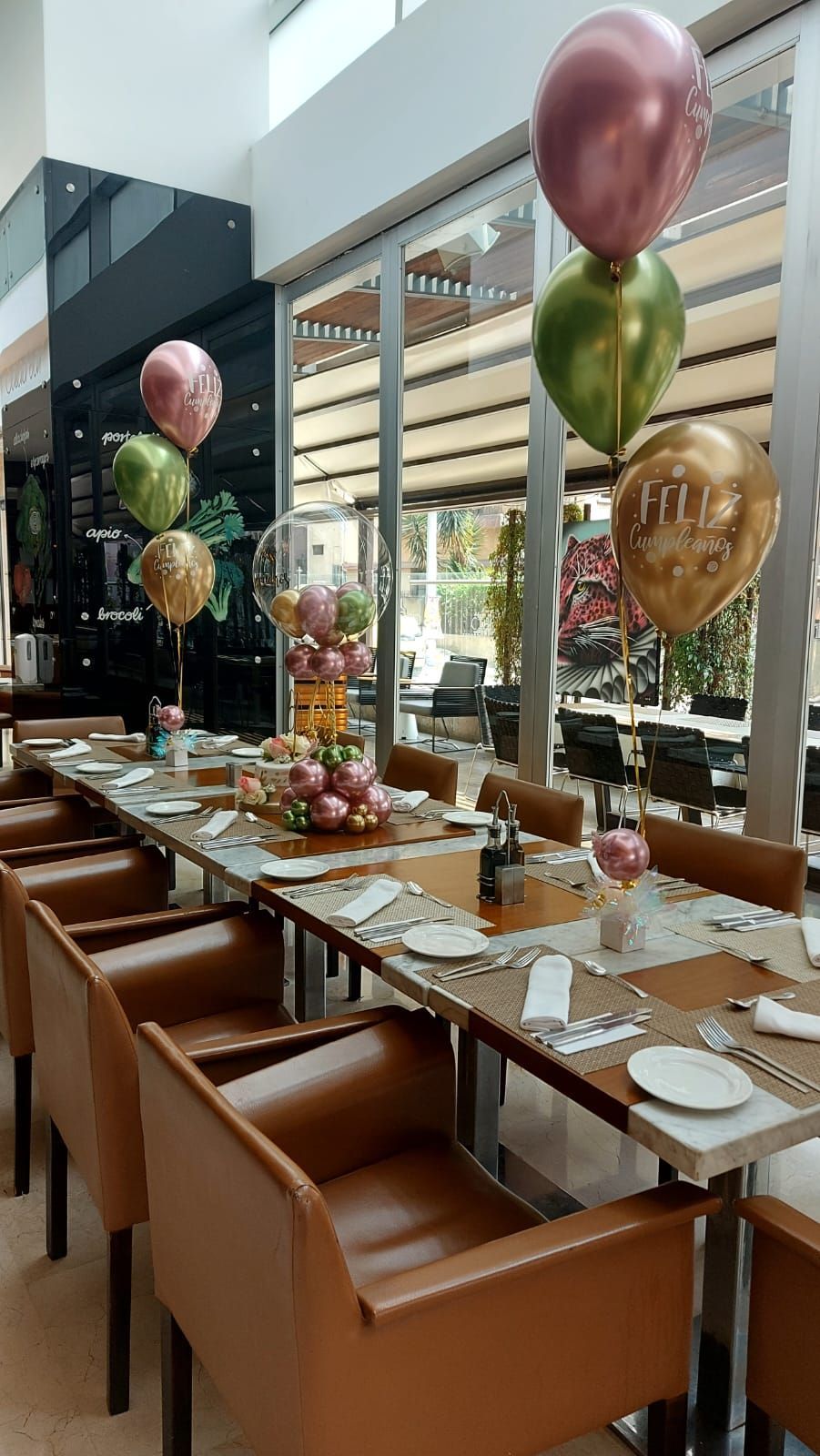 Mesa larga puesta con cubiertos, decorada con globos en un ambiente de restaurante.