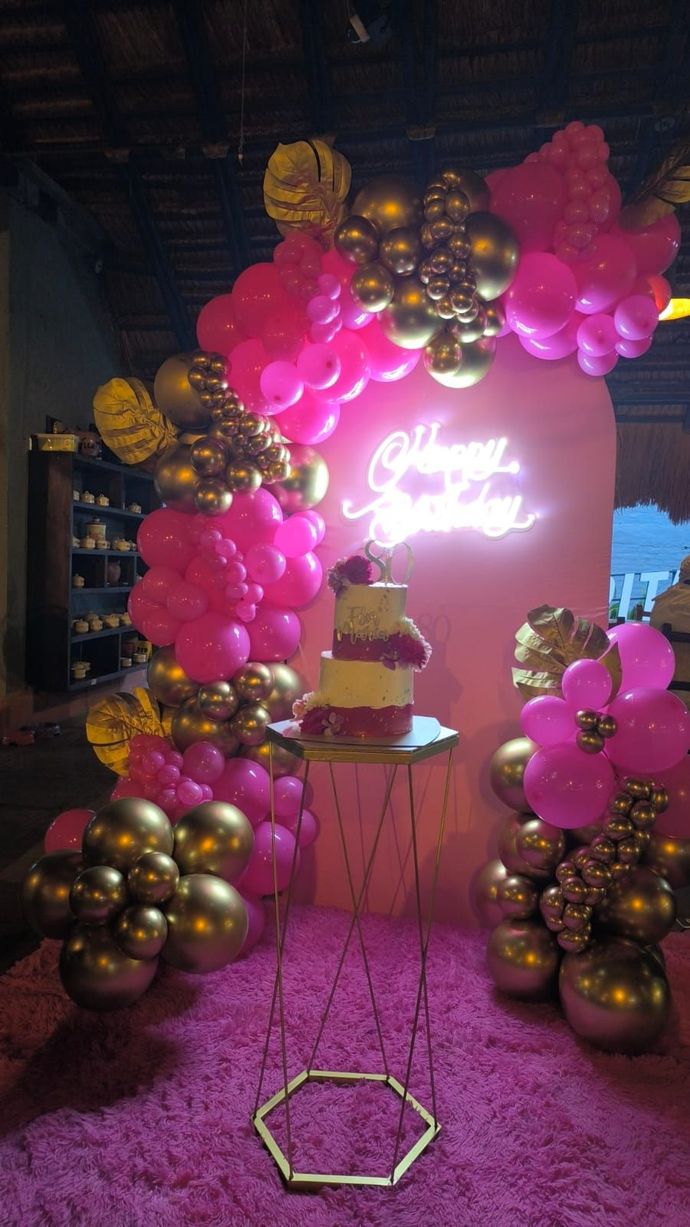 Decoración de fiesta de cumpleaños en rosa y dorado: pastel sobre un soporte, arco de globos, letrero de neón y alfombra rosa afelpada.