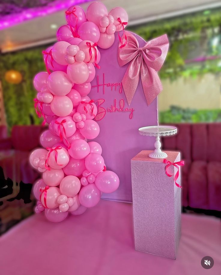 Telón de fondo rosa para fiesta de cumpleaños con globos, lazo y mesa con pedestal.