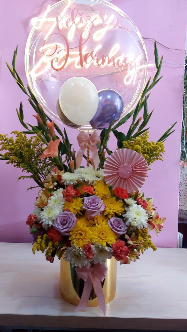Arreglo floral de cumpleaños con globos y letrero de neón en un jarrón dorado.