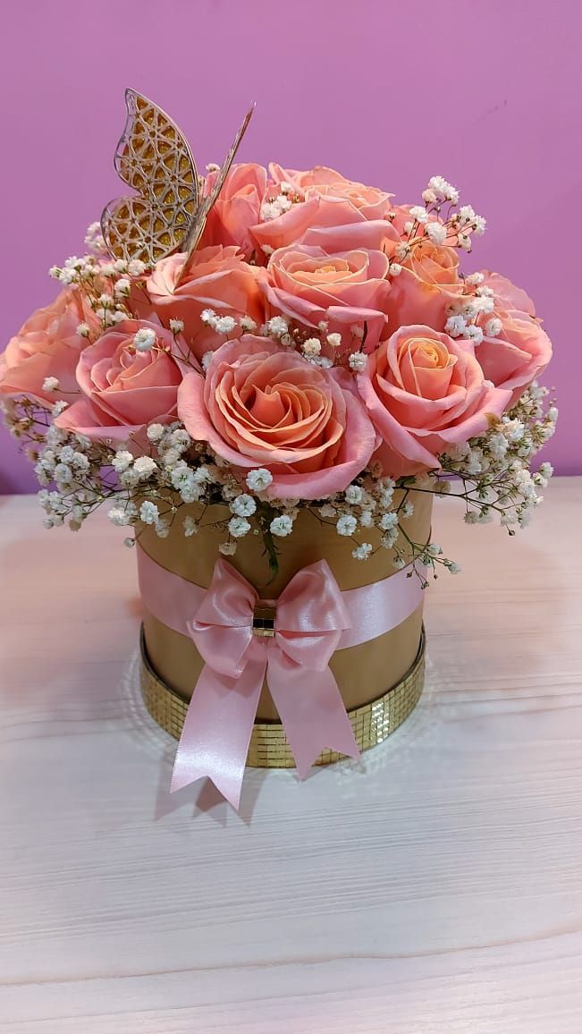 Rosas rosas en una caja redonda, atadas con una cinta rosa y decoradas con una mariposa dorada.