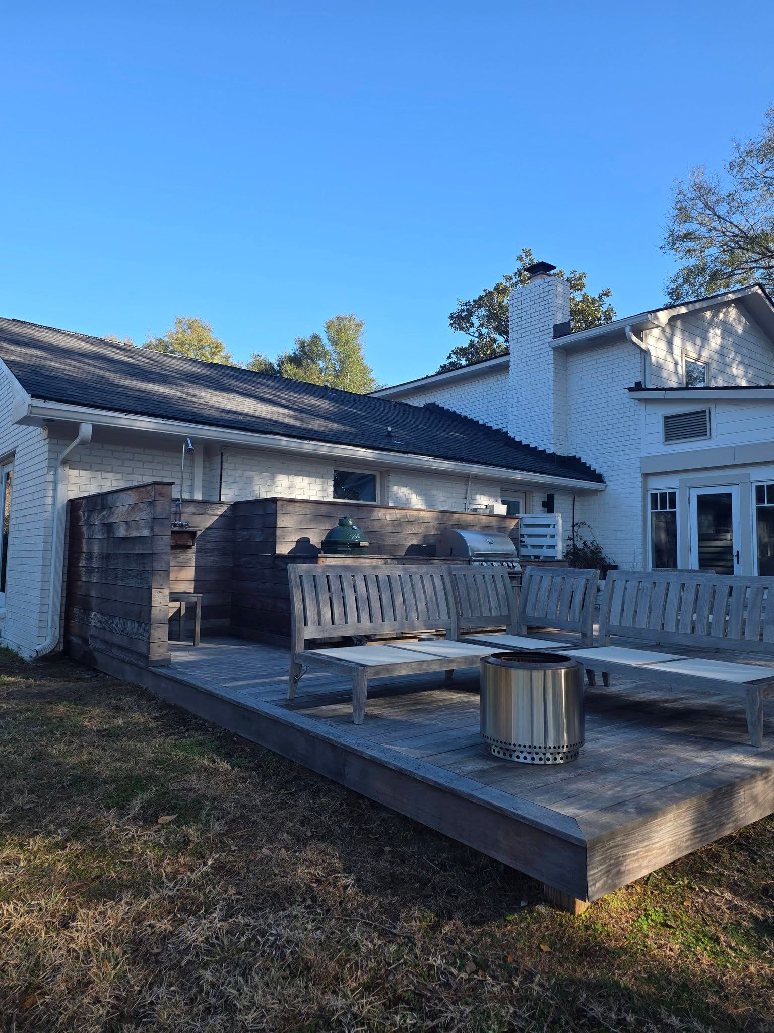White house patio with wooden lounge chairs, outdoor seating, and blue sky overhead
