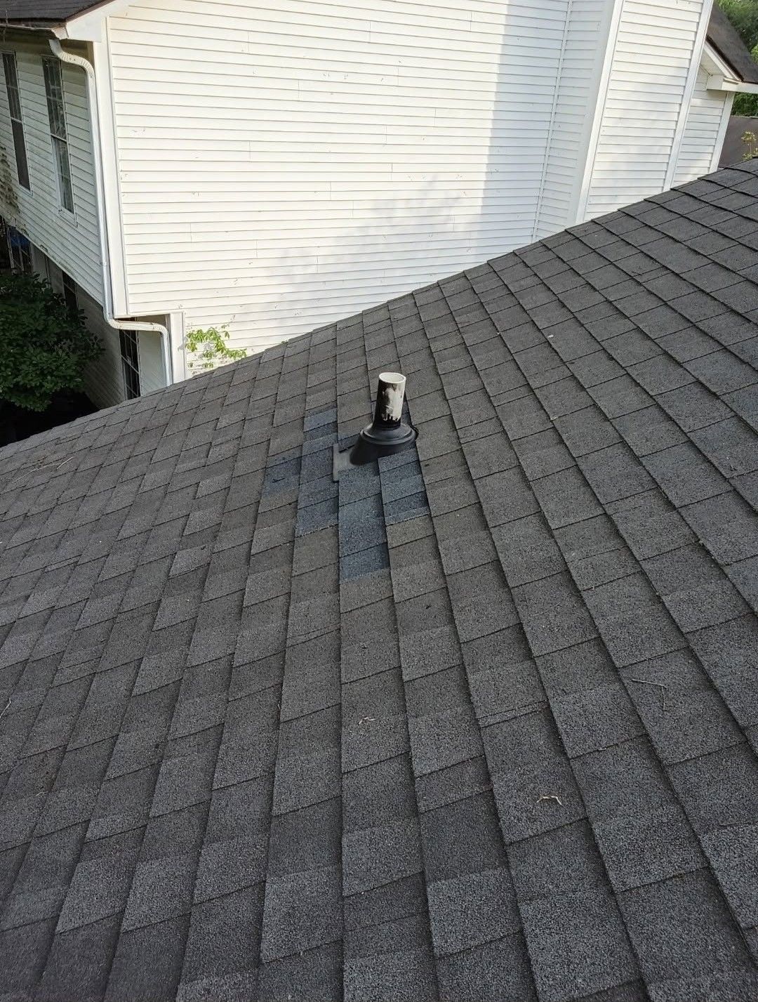Roof shingles with a small roof vent near a white house wall