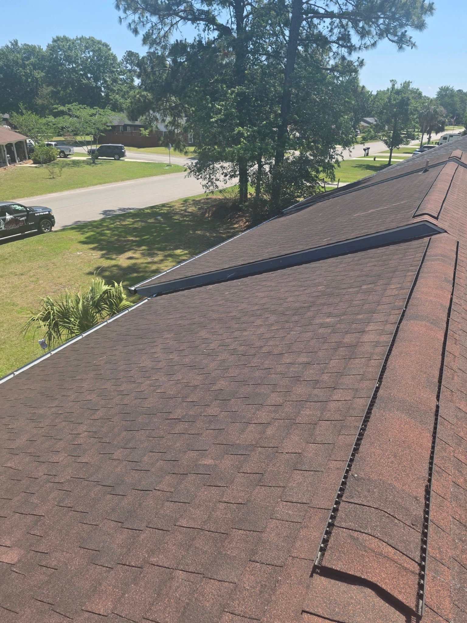 Brown shingle roof viewed from above, with a tree-lined street and parked cars beyond