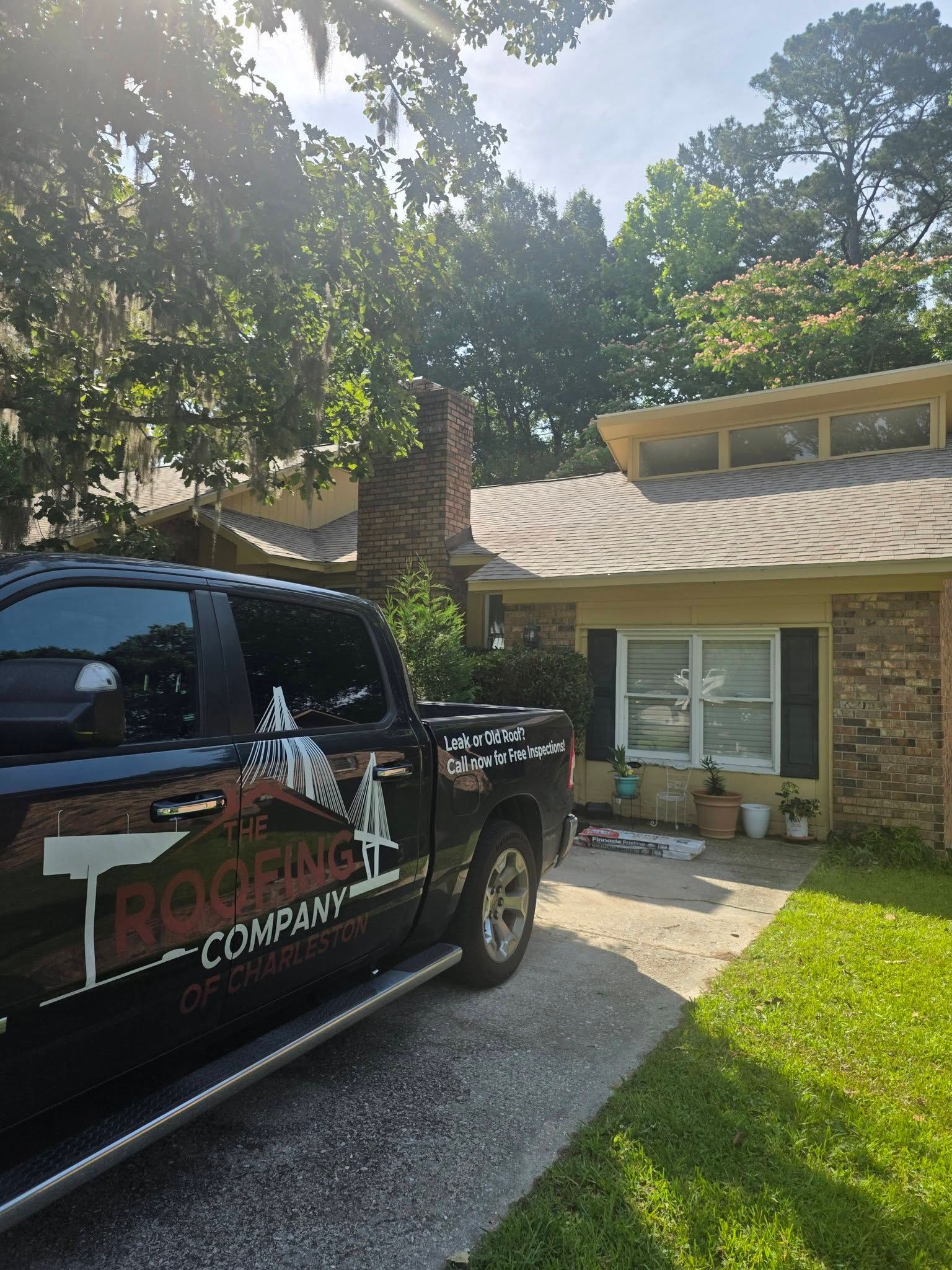 Black pickup truck with company logo parked beside a brick house on a sunny driveway