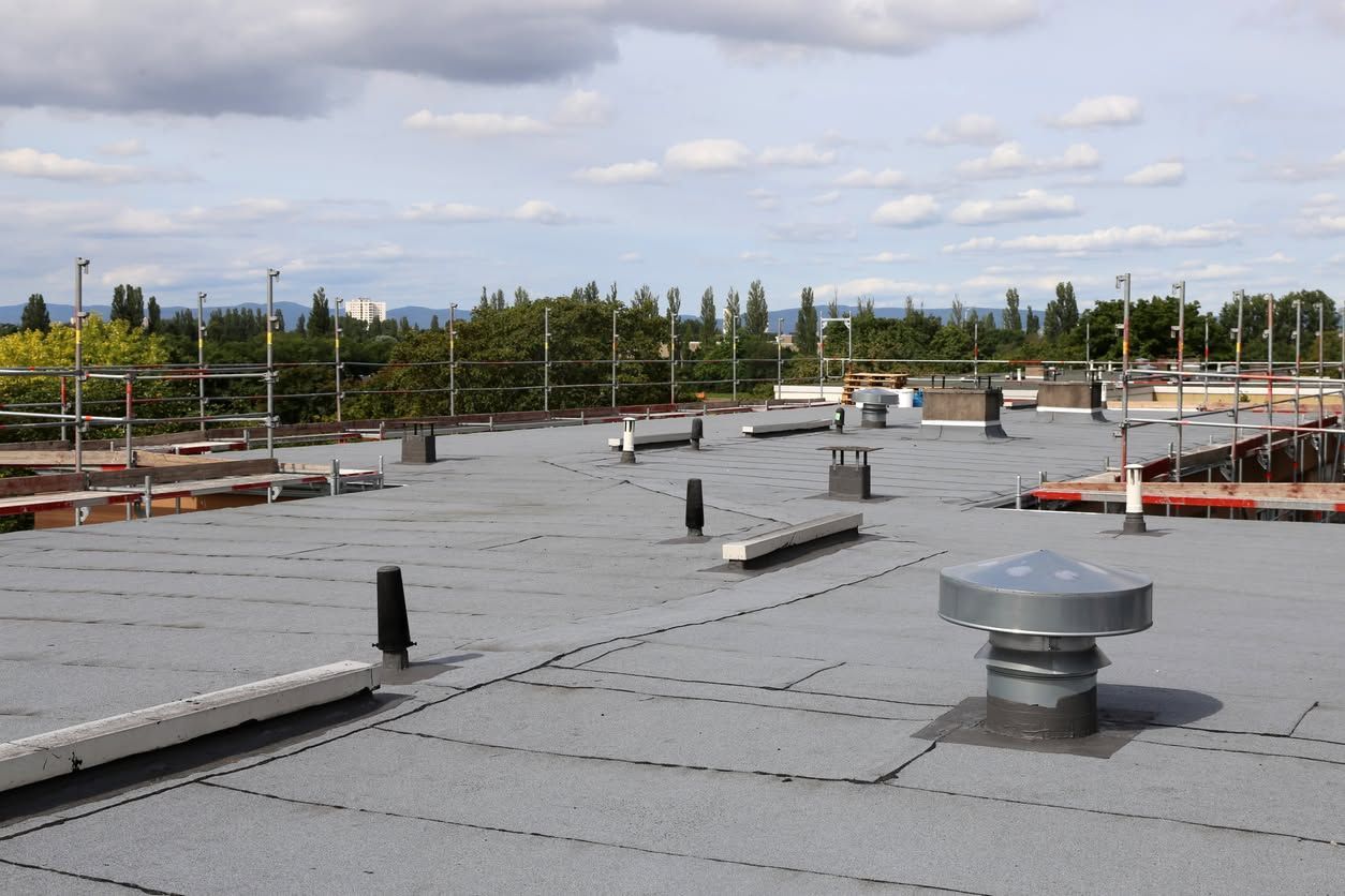 Flat rooftop with gray membrane, vents, and safety railings under a cloudy sky