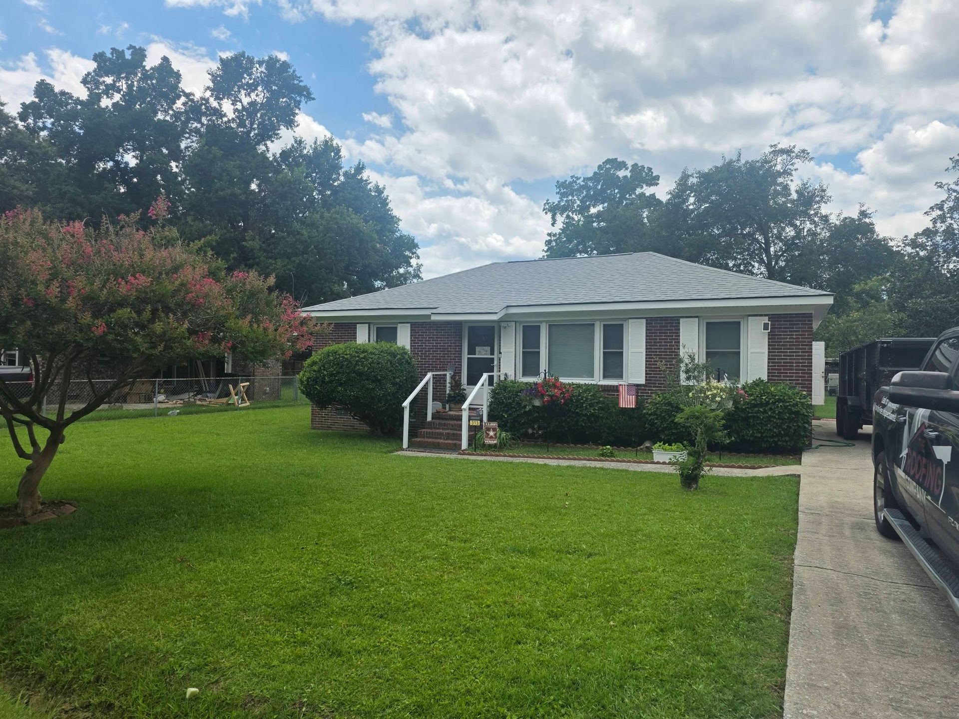 Single-story brick house with white trim, green lawn, and a driveway under a cloudy sky.