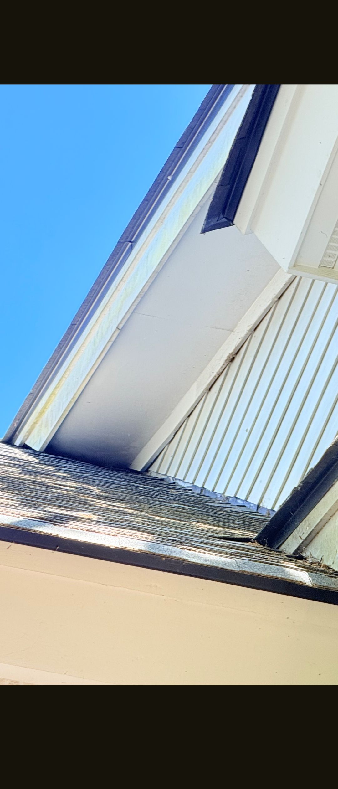 Upward view of a white house eave and roofline against a bright blue sky