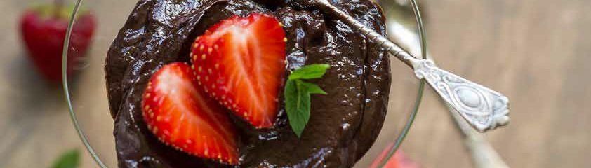 Chocolate dessert with sliced strawberries and a sprig of mint in a glass, with a silver spoon.