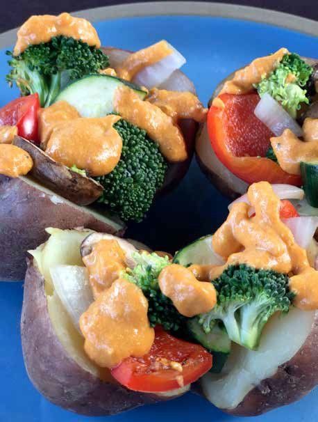Baked potatoes loaded with broccoli, red peppers, zucchini, and a creamy orange sauce, served on a blue plate.