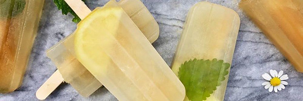 Lemon and mint popsicles arranged on a marbled surface with a daisy in the background.