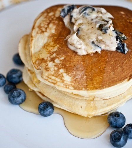 Stack of pancakes topped with butter and blueberries, served with maple syrup on a white plate.