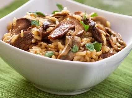 Mushroom risotto in a white square bowl, garnished with green herbs on a green surface.