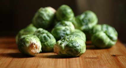 Pile of fresh green Brussels sprouts on a wooden cutting board, with a dark background.