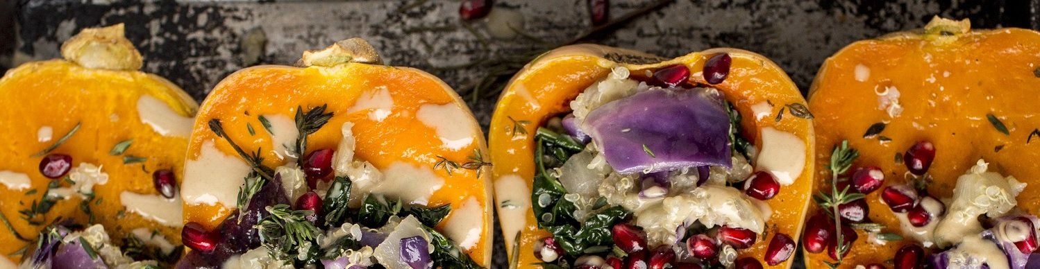 Roasted gourds filled with a purple vegetable, greens, and pomegranate seeds, garnished with sauce.