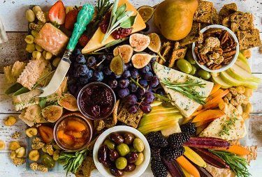 Charcuterie board with a variety of cheeses, fruits, crackers, nuts, olives, and dips.