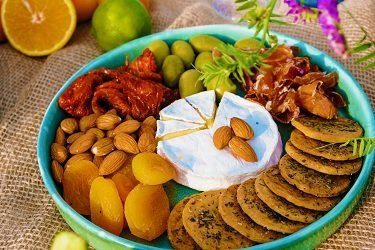Charcuterie board with cheese, almonds, apricots, olives, crackers, and dried tomatoes arranged on a blue plate.