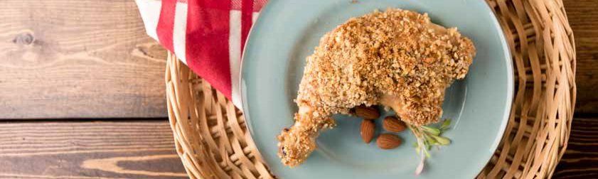 A breaded chicken leg on a blue plate with almonds. It rests in a woven basket next to a red-and-white striped napkin.