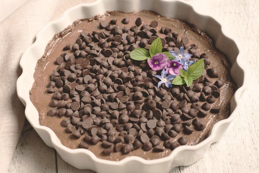 Chocolate dessert pie in a white fluted dish, topped with chocolate chips and flowers.
