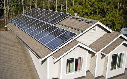 Solar panels installed on a residential roof, angled toward the sun. The house is light-colored with brown roofing.