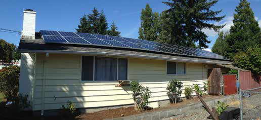 A yellow house with solar panels on the roof and trees in the background under a blue sky.