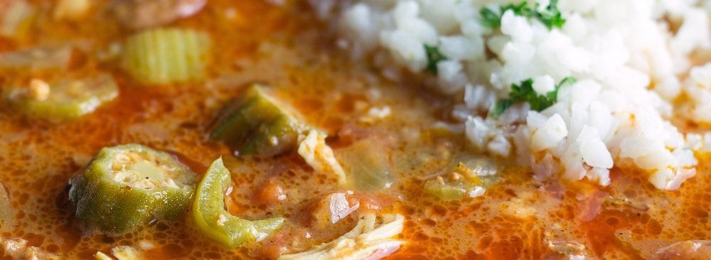 A close-up of gumbo with okra and a side of white rice garnished with green herbs.