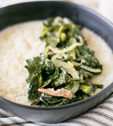Bowl of creamy grits topped with sauteed collard greens and onions; dark bowl on a striped cloth.