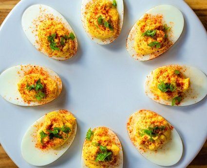 Deviled eggs arranged in a circle on a white plate, garnished with paprika and chopped herbs.