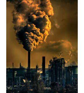 Factory emitting thick, orange-brown smoke into a hazy, polluted sky. Industrial setting with dark silhouettes of buildings and smokestacks.
