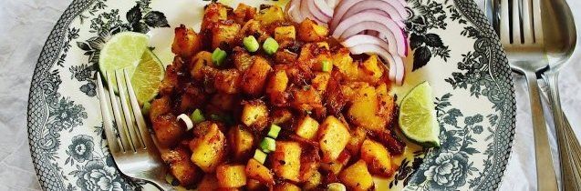 A plate of diced food with red onions, lime, and green onions on a decorative plate. A fork and spoon are on the right.