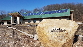 Indian Creek Nature Center building with solar panels on the green roof and a large stone sign in front.